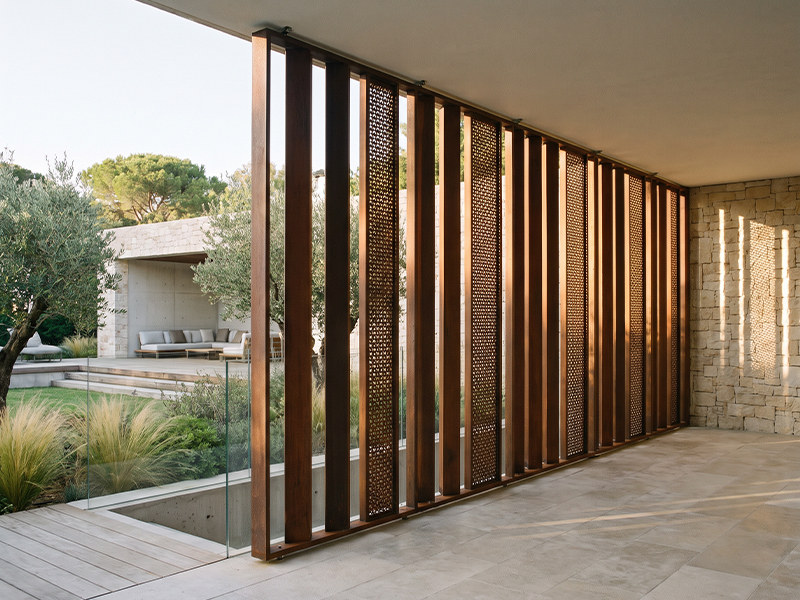 Claustra vertical en acier Corten avec panneaux perforés installé comme brise-soleil dans une villa contemporaine