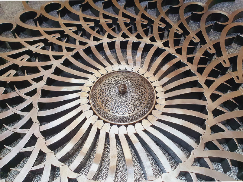 Vue rapprochée d’une œuvre murale décorative en métal finition laiton avec motif radial géométrique