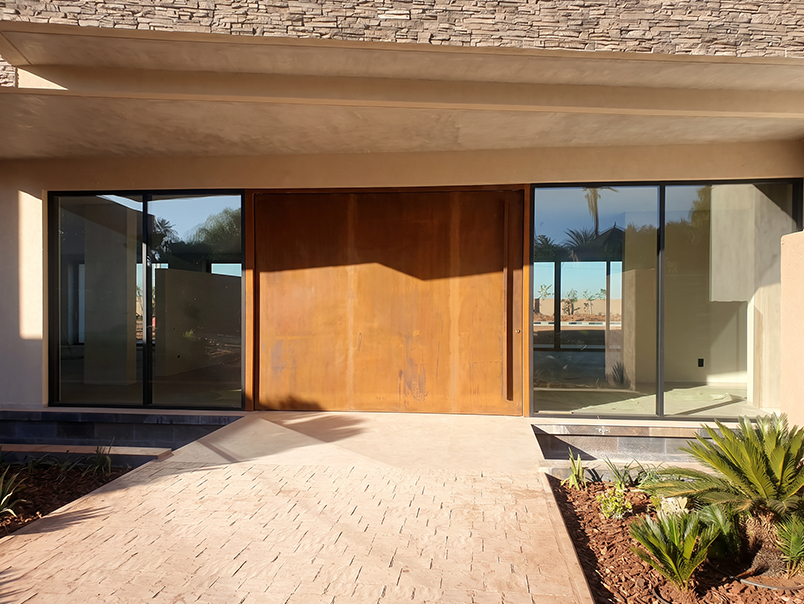 Entrée contemporaine de villa avec grande porte en acier Corten entre deux façades vitrées