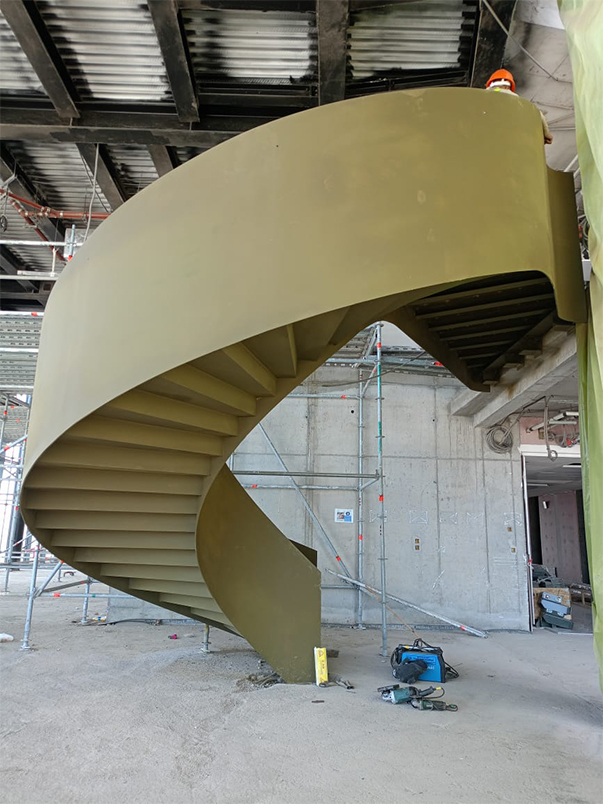Escalier hélicoïdal métallique sur mesure installé dans un bâtiment en construction avec structure courbe visible