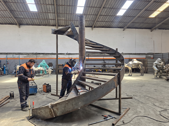 Soudeurs JOJMA fabriquant et assemblant un escalier métallique hélicoïdal sur mesure dans l’atelier.