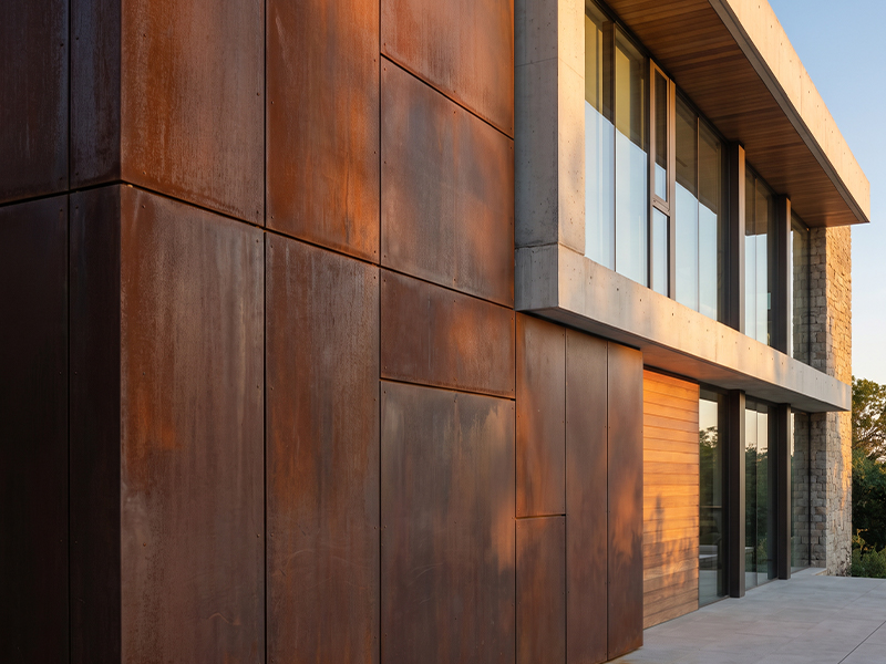 Façade contemporaine de villa habillée de grands panneaux en acier Corten avec vitrage et béton apparent