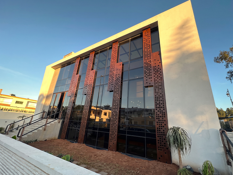 Entrée d’un bâtiment contemporain avec grands panneaux verticaux en acier Corten perforé devant une façade vitrée