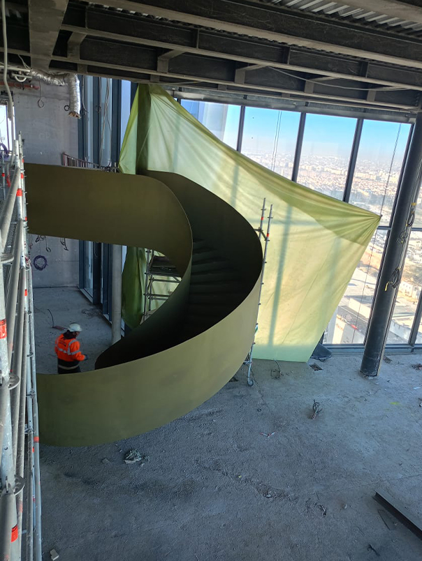 Escalier hélicoïdal métallique monumental en cours d’installation dans un étage vitré de la Tour Mohammed VI