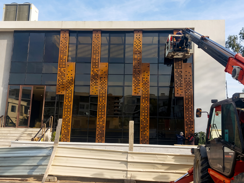 Installation de grands panneaux perforés en acier Corten sur une façade vitrée à l’aide d’une nacelle