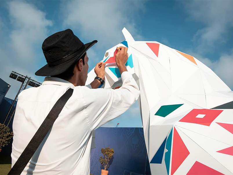 Artiste appliquant un motif graphique coloré sur une sculpture de cheval JOJMA.