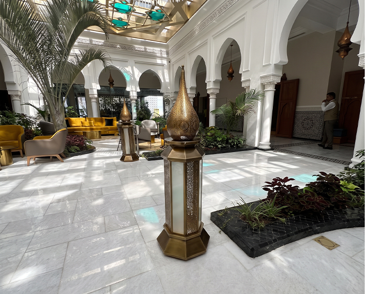 Lanternes décoratives marocaines en laiton installées dans un patio intérieur avec arches, colonnes et végétation