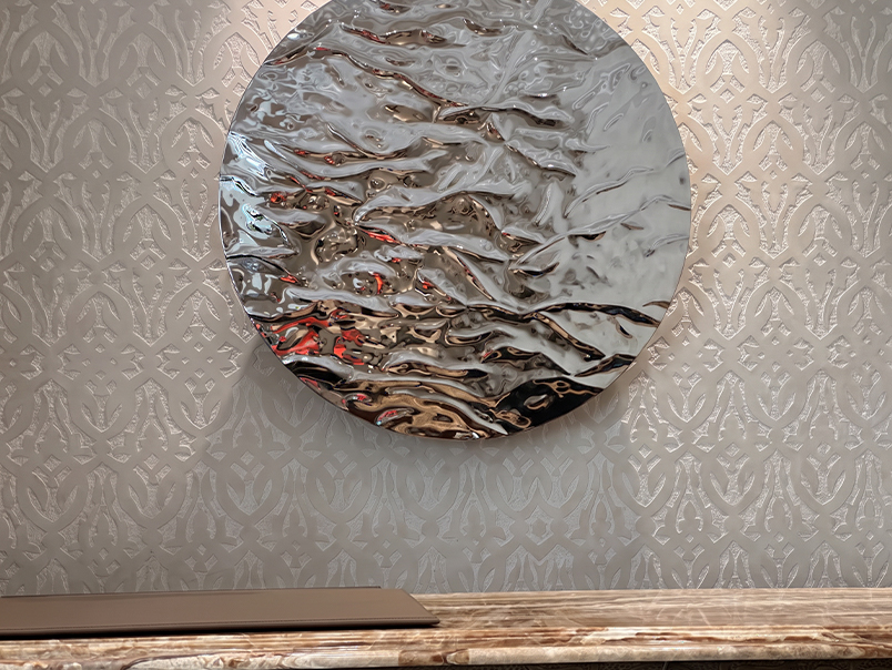 Œuvre murale circulaire en inox poli à surface texturée et réfléchissante intégrée dans un intérieur haut de gamme