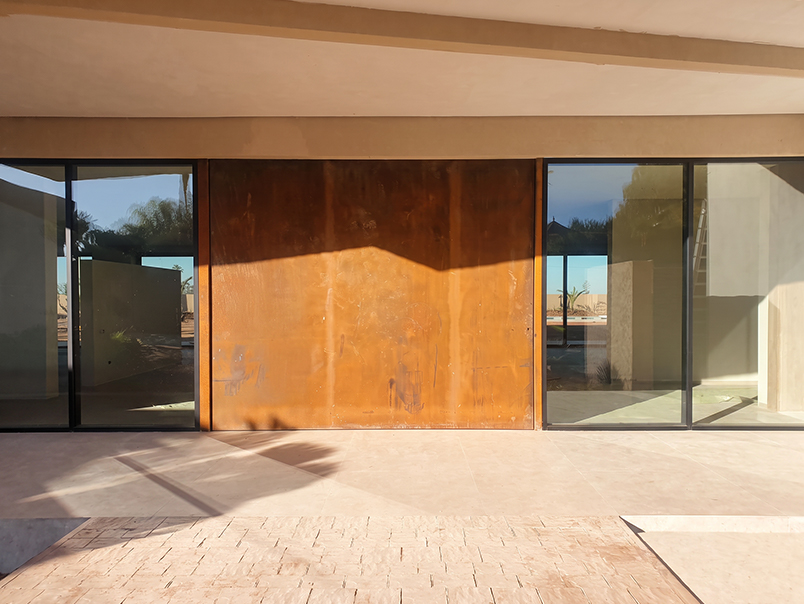 Porte monumentale en acier Corten fermée intégrée à une façade de villa avec baies vitrées