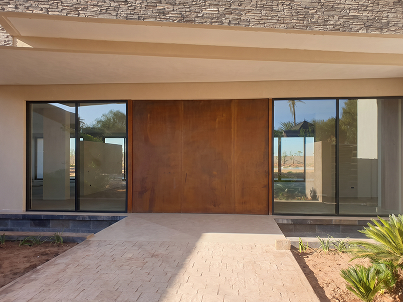 Grande porte pivotante en acier Corten intégrée à la façade vitrée d’une villa contemporaine