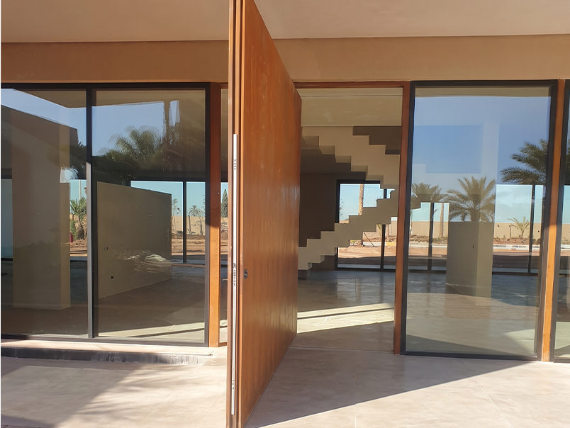 Grande porte pivotante en acier Corten ouverte donnant accès à l’intérieur d’une villa contemporaine