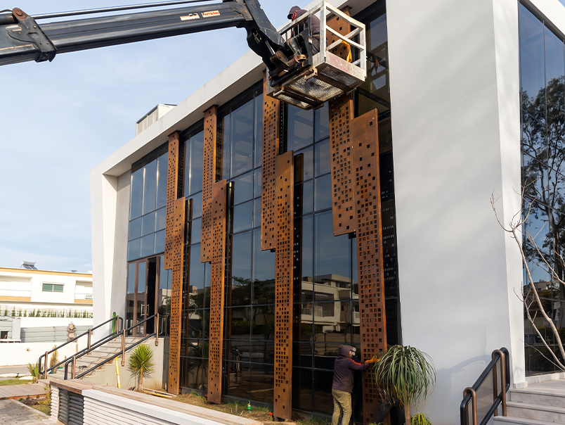 Techniciens installant et réglant des panneaux perforés en acier Corten sur une grande façade vitrée
