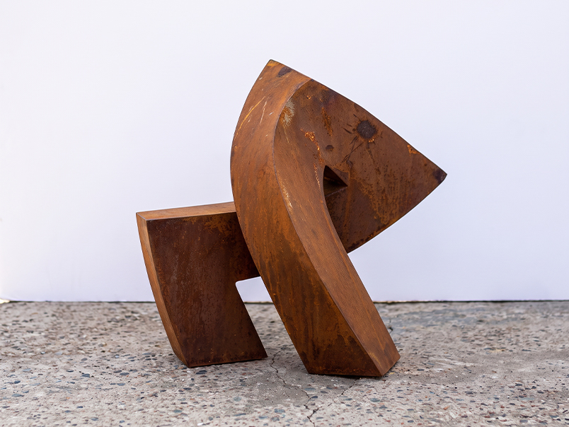 Vue latérale d’une sculpture abstraite en acier Corten avec volumes angulaires et finition patinée
