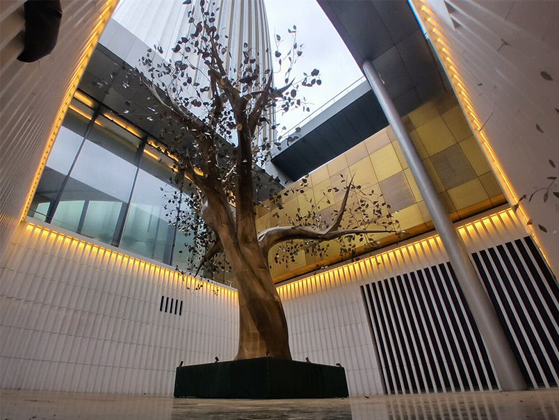 Sculpture monumentale représentant un arbre en métal installée dans un grand atrium architectural contemporain