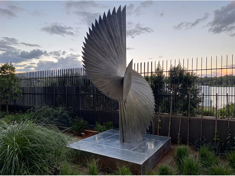 Sculpture monumentale en inox composée de lames métalliques évoquant des ailes dans un jardin contemporain