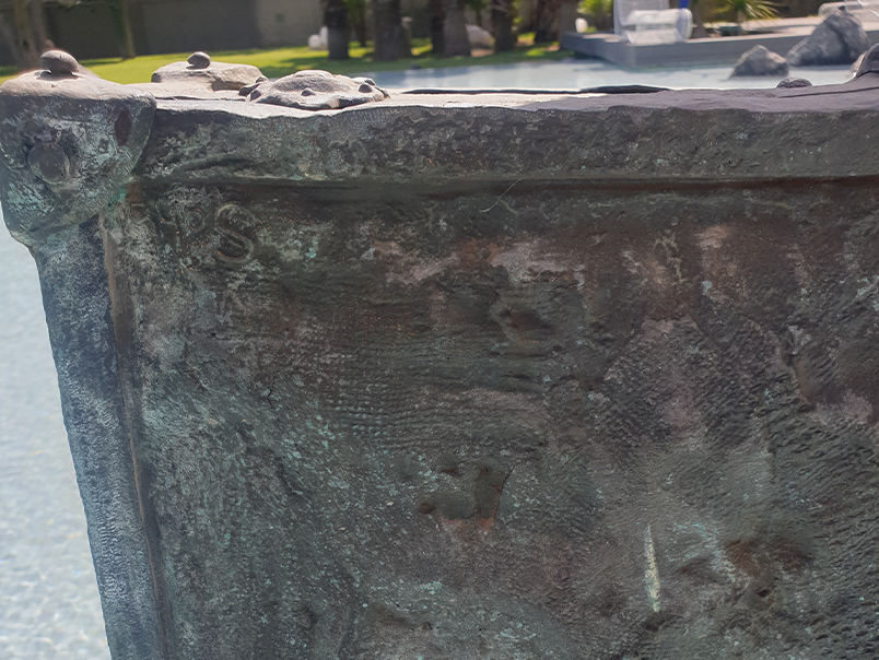 Gros plan sur la texture patinée et les détails de surface de la valise de la Sculpture Peigne
