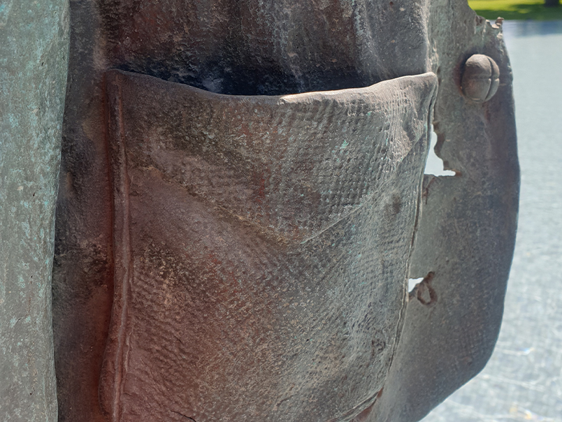 Gros plan sur une poche et les textures du vêtement de la Sculpture Peigne en bronze patiné