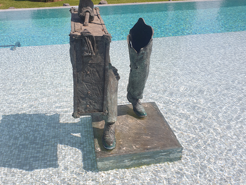 Sculpture figurative en bronze patiné avec jambes fragmentées et valise près d’un bassin
