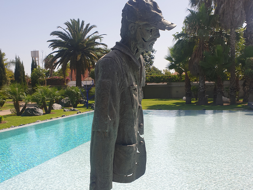 Vue de profil de la Sculpture Peigne représentant un personnage en bronze patiné près d’un bassin