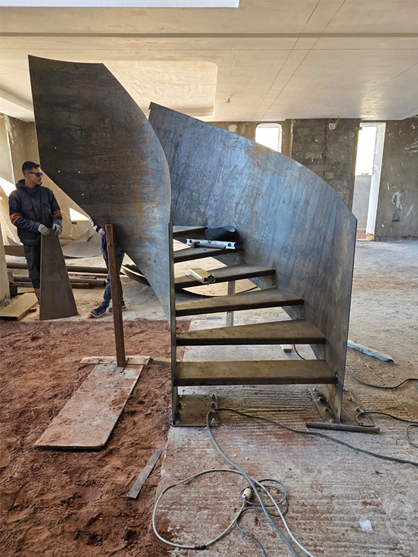 Structure brute en acier d’un escalier hélicoïdal avec marches métalliques dans une villa en chantier